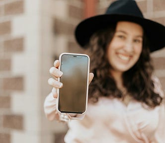 With a fashionable hat on, an overweight woman happily displays her cell phone