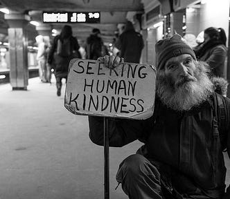 Man holding sign reading “seeking human kindness.” An expression of the consistent life ethic