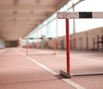 Close up of a hurdle with a runner in the far distance, blurred.