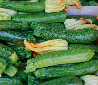 Closeup of stacks of zucchini with their flowers still attached for sale at a produce market.