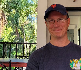 Picture of male author wearing a NY Mets hat with palm trees in the background inCosta Rica.