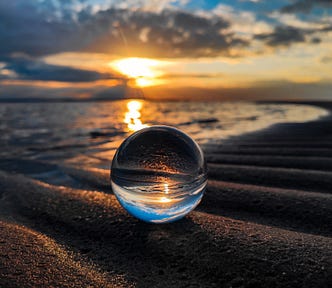 A water droplet reflects a scene of sunset over the ocean.