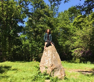 Girl meditating atop a rock surrounded by green trees