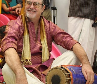 Me, sitting cross-legged with fancy clothes & a drum from India