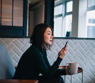 A photo of an Asian woman looking at her phone, cup in hand.