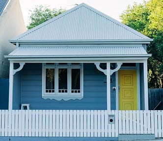 A wooden cottage painted blue with a yellow door.