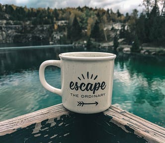 coffee mug saying “escape the ordinaty) on a handrail overlooking a beautiful mountain lake