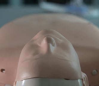 A CPR manikin lying face up on a grey floor