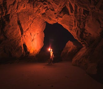 Man lifts up a red flare light inside a cave.