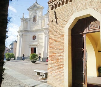 Italian plaza in alba, italia taken from a coffee shop called caffe vergnano. White historic church, sunny day, brick building.