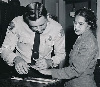 A Black woman (Rosa Parks) is seen standing on the right. A sheriff, seen standing on the left, is fingerprinting her left hand.