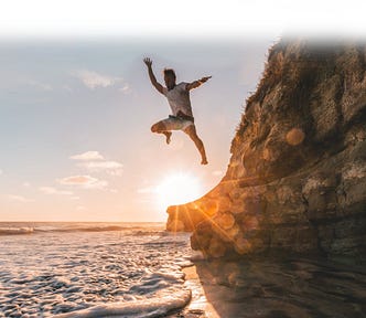 A guy jumping off a cliff into the water at sunset