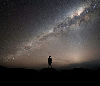 sillhouette of a human looking up at the vastness of a starry night sky (resilience, optimism)
