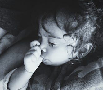 Black and white photo of a toddler, eyes closed, sucking her thumb