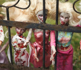 A group of Barbie dolls standing behind a fence. The dolls are painted and dressed to resemble zombies, with bloody hands and mouths.