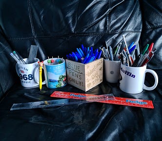 Boxes of pens and pencils, and two rulers, on a black sofa