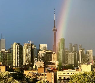 Skyline of Toronto with the CN Tower in the middle and a bright rainbow coming down in front of the Tower