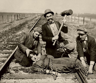 Mabel Normand being tied to the tracks in the silent film Barney Oldfield’s Race for a Life (1913). The image is available at https://commons.wikimedia.org/wiki/File:Barney_Oldfield%27s_Race_for_a_Life.jpg.