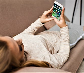woman laying on couch looking at cell phone