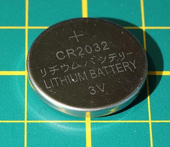 Small 3V button battery on a green background with yellow checks.