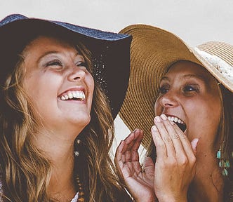 Two young women in knit dresses and floppy hats talking and laughing