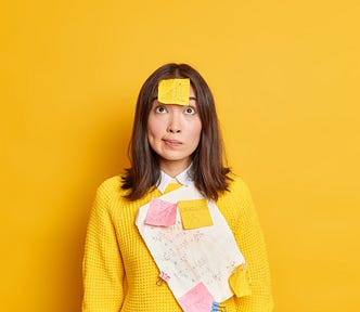 A serious female has a post-it note stuck on her forehead and looks as if she is thinking about a memoir. Bright yellow background.