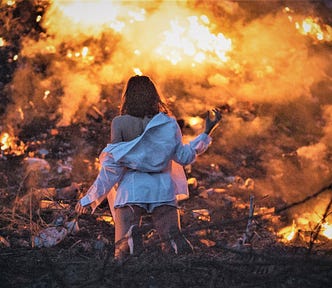 rear view of woman wearing white top off the shoulder staring at burning landscape