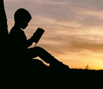 A kid, sitting in a twilight and staring into an open book