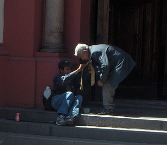 older man bends over to help a man prone on the steps of a church in Santiago Chile
