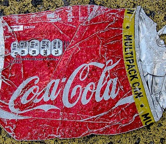 Color photo of a Coca-Cola can that has been crushed, lying on the road.