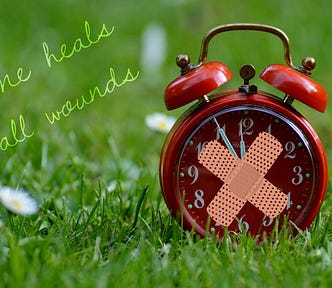 Image of an old-fashioned red alarm clock on the grass with two plasters stuck to it in a cross on the front, and to the left of it are the words: time heals all wounds.