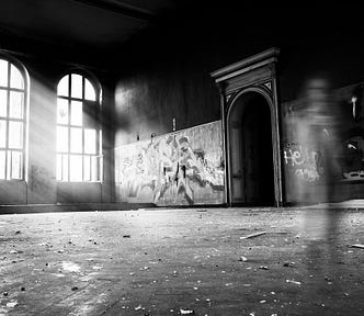 A photo of a large room, perhaps in an old school, were blurred images of beings are moving.