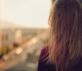 photo of a woman with her back turned to the camera. she seems to be staring out a window or balcony, but the background landscape is out of focus