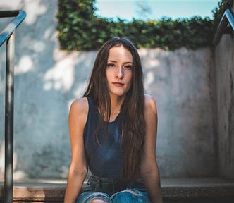 girl with long brown hair wearing blue sleeveless top sitting on concrete steps