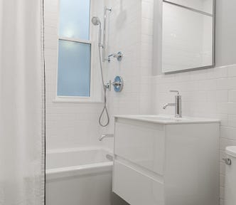 Plain white bathroom with toilet, sink, and shower.