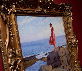 Close up of gold frame against a red wall, showing a painting of a woman in a red dress on a rock, looking out to sea