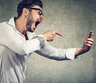 A man with his phone in one hand, screaming at it and pointing his finger at it