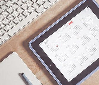 Part of a keyboard, a pad and pencil, and a calendar app on a tablet