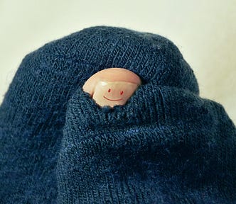 Image of a big toe with a smiley face painted on it, poking out of a hole in a woolen sock