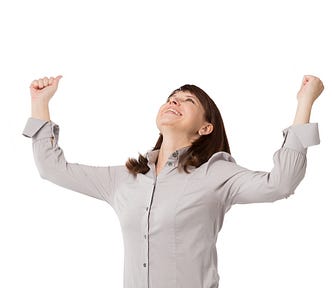 Woman with shoulder length hair and wearing smart blouse has her arms up and open in a gesture of achievement or excitement