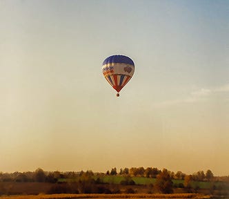 View of a hot-air balloon rising over a farmer’s field