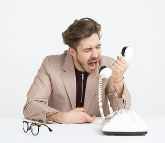 Young white man in a tan suit screaming into a white phone.