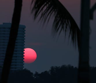 The pink moon rising partially obscured by a building