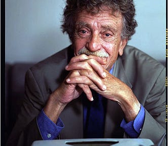 Writer Kurt Vonnegut seated in front of a typewriter with his hands clasped