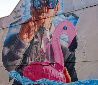 A mural of a man with sunglasses blowing up a pink inflatable flamingo.