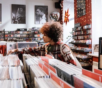 A woman in a curly fro looks through vinyl records at a record store.