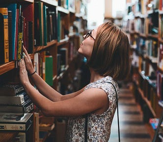 Woman in bookstore looking up at a higher shelf full of books.