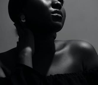 A woman with a headwrap on stares into the distance. The picture is black and white.