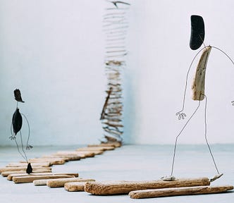 Sculpture by artist Anne Cécíle de Bretagne, small driftwood figurines walking towards an endless ladder on the other side of the room.