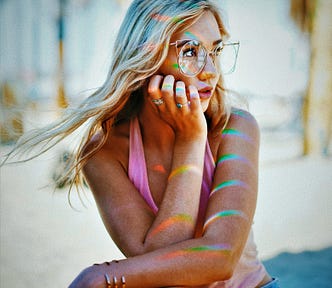 girl with long blonde hair wearing glasses and holding hand under her chin